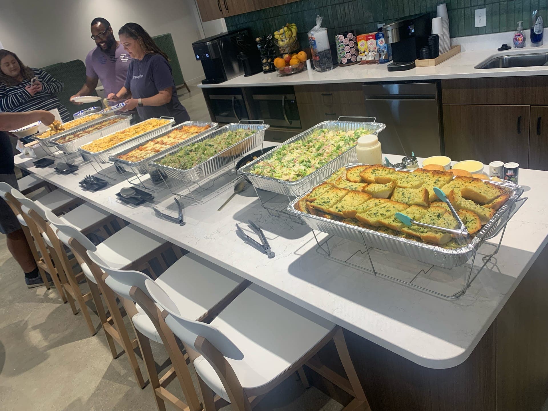 A Hauling Eats catering spread — trays of pasta and salads with fresh garlic bread, set out and ready to serve at an event.